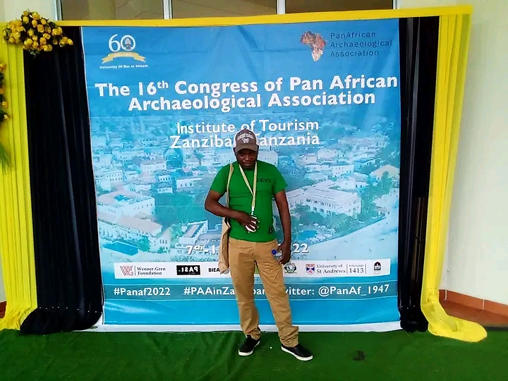 The Executive Director of the KEYS Organization in front of the photo wall of the 16th PANAF congress.